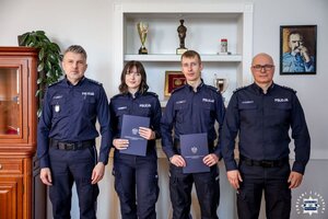 Dwoje policjantów w Gabinecie Komendanta Wojewódzkiego Policji w Kielcach wspólnie z bezpośrednim przełożonym i szefem kieleckich policjantów pozują do zdjęcia.