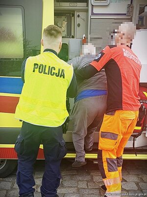 policjant i ratownik pomagają wejść seniorowi do karetki.