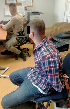 mężczyzna siedzi na krześle, obok inny mężczyzna policjant.