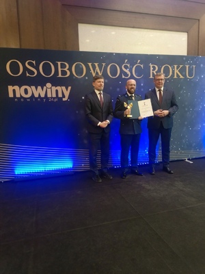 Uhonorowany policjant wraz z dwoma mężczyznami w garniturach pozują do zdjęcia.