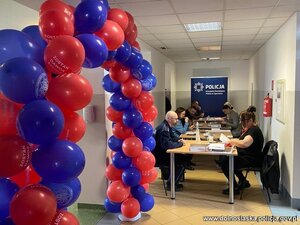 Kobiety siedzą za stołem , pobierany patyczkiem materiał genetyczny. Widać logo policji i fundacji DKMS