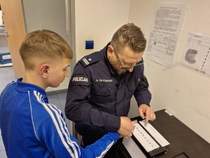 chłopiec wchodzi do komisariatu policji, wita go policjant, chłopiec przymierza stroje policyjne, robi sobie zdjęcia.