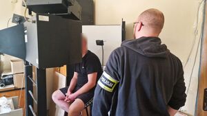 Mężczyzna oddaje odciski palców. Prowadzony jest przez policjantów.