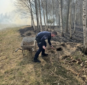 Policjant nakłada piasek na taczkę.