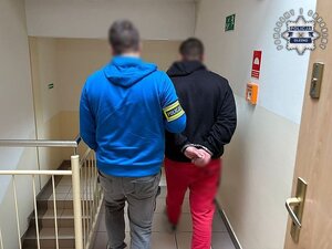 Policja prowadzi zatrzymanego. Wybita szyba, instalacja elektryczna.