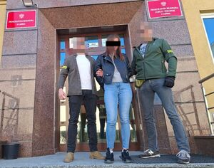 Policjanci prowadzą zatrzymaną kobietę.