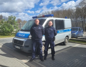 policjanci stoją przy radiowozie.
