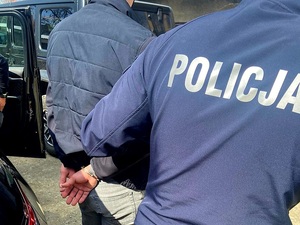 Zatrzymany w kajdankach prowadzony przez policjanta.