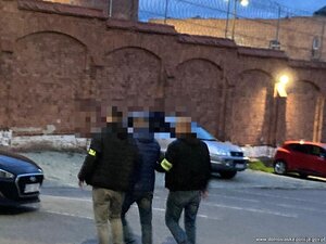 policjanci prowadzą zatrzymanego. Papierosy bez akcyzy leżą porozkładane w kartonach.