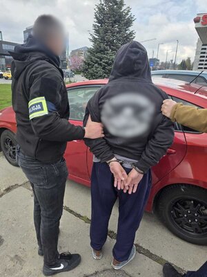 Policjanci trzymają zatrzymanego zakutego w kajdankach.