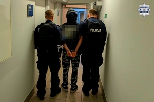 Policjanci prowadzą korytarzem zatrzymanego.