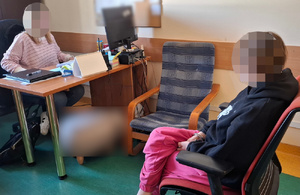 policjant siedzi przy biurku, naprzeciwko siedzi zatrzymana kobieta.