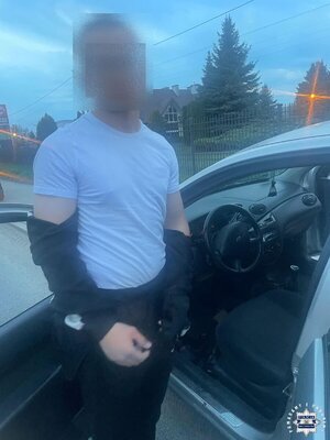 Zatrzymany mężczyzna stoi przy samochodzie osobowym, który ma otwarte drzwi od strony kierowcy.