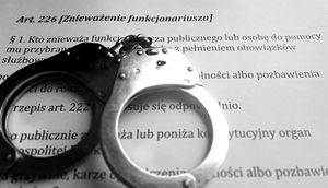 Kajdanki leżą na otwartym kodeksie karnym na stronie z Artykułem 226 (znieważenie funkcjonariusza).