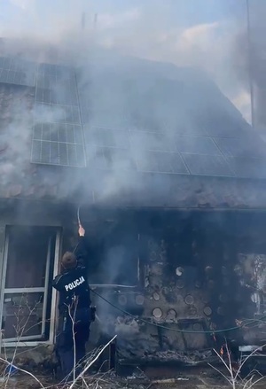 Policjant gasi pożar budynku.
