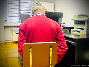 mężczyzna siedzi na krześle, ma ręce skute kajdankami.