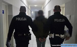 Dwaj policjanci prowadzą korytarzem zatrzymanego.