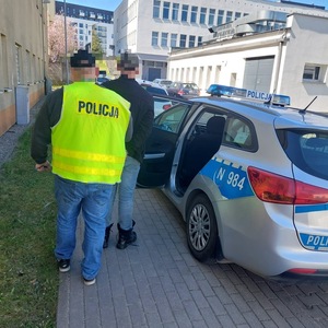 Policjant prowadzi zatrzymanego do radiowozu.