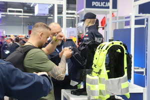 Zdjęcie przedstawia eksperta z obszaru uzbrojenia i techniki policji, przedstawiającego zainteresowanym nowoczesne kamizelki kuloodporne dedykowane policjantom komórek patrolowo-interwencyjnych oraz ruchu drogowego