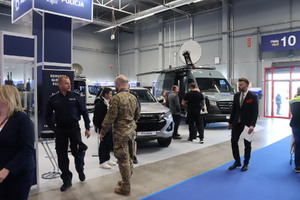 Zdjęcie przedstawia ludzi zwiedzających stoisko Policji oraz pojazd Mercedes Benz Sprinter pełniący funkcję Mobilnego Punktu Dystrybucyjnego Infrastruktury Teleinformatycznej