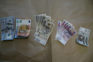 Pieniądze porozkładane na stole. Widać złote sztabki, łańcuszki, pierścionki i pieniądze w tym dolary, euro.