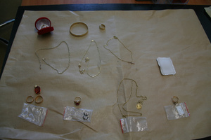 Pieniądze porozkładane na stole. Widać złote sztabki, łańcuszki, pierścionki i pieniądze w tym dolary, euro.