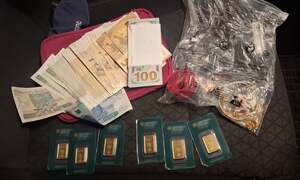 Pieniądze porozkładane na stole. Widać złote sztabki, łańcuszki, pierścionki i pieniądze w tym dolary, euro.