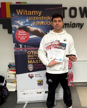 Policjant pozuje do zdjęcia z dyplomami i medalami.