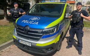 Dwaj policjanci stoją przy radiowozie.