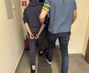 Na zdjęciu nieumundurowany policjant prowadzi zatrzymanego w kajdankach.