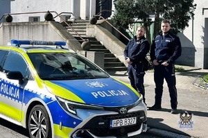 Dwaj policjanci stoją przy radiowozie.