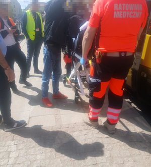 Poszkodowana kobieta na noszach. Ratownik medyczny i inne osoby.