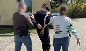 Policjant i policjantka prowadza zatrzymanego mężczyznę.