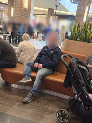 Mężczyzna siedzi na siedzisku na terenie galerii handlowej.