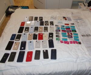 Łóżko a na nim kilkadziesiąt telefonów komórkowych i kart płatniczych.