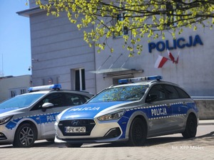 Dwa policyjne radiowozy stojące przed budynkiem Policji.