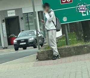 Mężczyzna z plecakiem stoi na ulicy patrząc na ekran smartfona.