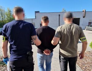 Dwaj policjanci prowadza zatrzymanego mężczyznę.