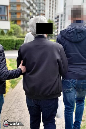 plecy starszego mężczyzny, obok prowadzą go dwaj policjanci.
