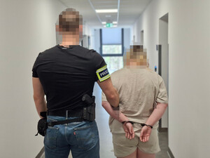 Policjant prowadzi korytarzem kobietę - widok z tyłu.