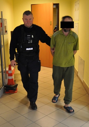 Policjant prowadzi zatrzymanego mężczyznę.