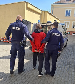 dwóch policjantów prowadzi zatrzymanego.