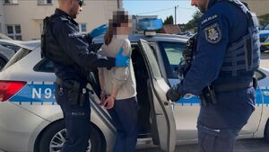 dwóch policjantów  prowadzi zatrzymaną do radiowozu.