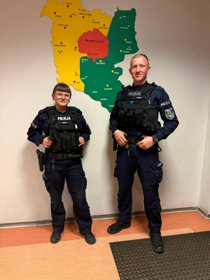 Policjant i policjantka stoją na tle ściany z mapą powiatu trzebnickiego.