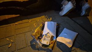 Na pierwszym planie leżące na ziemi odzyskane banknoty w kopertach, z tyłu widać buty policjanta, który trzyma zatrzymanego leżącego w kajdankach na ziemi.