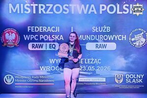 Policjantka w stroju sportowym z medalami na szyi i statuetką w dłoni.