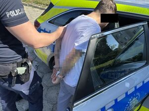 Zatrzymany wsiada do radiowozu. Z tyłu stoi policjant.
