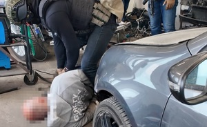 Zatrzymany leży na ziemi, przed samochodem, nad nim pochyla się policjant.