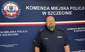 Policjant stoi na ścianie z napisem i logo Komendy Miejskiej Policji w Szczecinie.