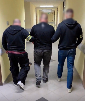 dwóch policjantów prowadzi zatrzymanego przez korytarz.
